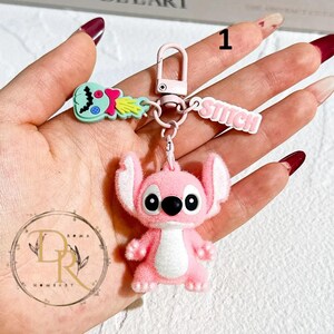 May include: A pink Stitch keychain with a matching clasp, a small green and blue alien charm, and a pink "Stitch" name tag. The keychain is a fun accessory for fans of the animated character.