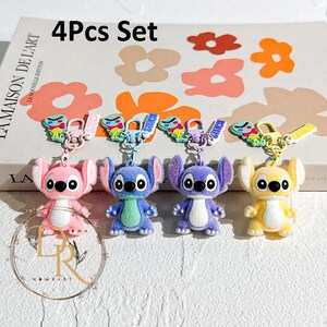 May include: A set of four character keychains in pink, blue, purple, and yellow. Each keychain features a cartoon character with large eyes and ears. The keychains are attached to a metal clasp and a small strap. The text "4Pcs Set" is visible.