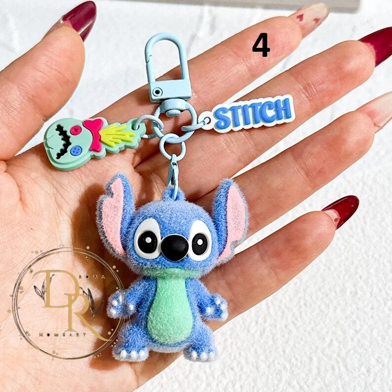 May include: A blue Stitch keychain with a matching blue clasp. The keychain features a plush Stitch figure, a green and pink alien, and a blue "Stitch" nameplate. The figure has large black eyes and a green belly.