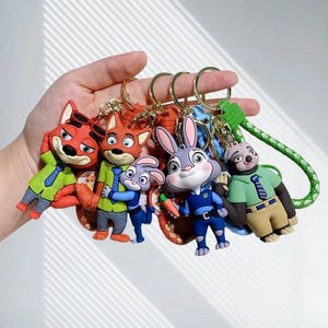 Può includere: Una collezione di portachiavi colorati dei personaggi di Zootropolis. I portachiavi presentano Nick Wilde, Judy Hopps e altri personaggi. Ogni portachiavi ha un anello color oro e un design dettagliato. I personaggi indossano i loro abiti distintivi.