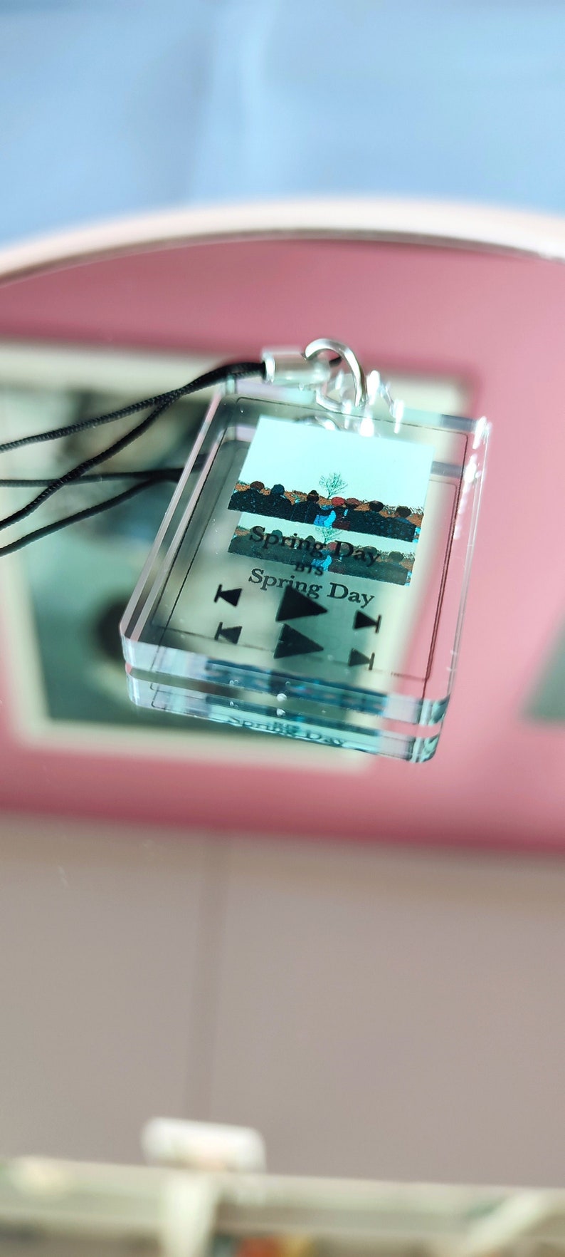 May include: A clear plastic keychain with a photo of a group of people and the text "Spring Day" and "BTS Spring Day". The keychain has a black cord and a silver ring.