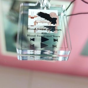 May include: A clear acrylic keychain with a black and white image of a bird with wings spread. The text "Blood Sweat and Tears BTS Blood Sweat and Tears" is printed on the keychain.