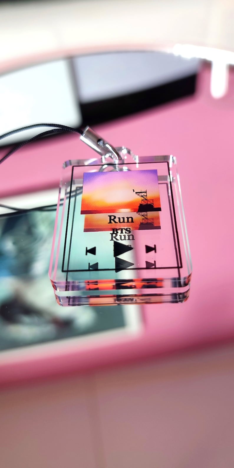 May include: A clear acrylic keychain with a colorful sunset image and the text "Run BTS Run". The keychain has a black lanyard and a silver metal ring.