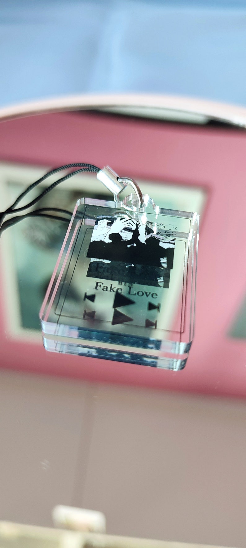 May include: A clear acrylic keychain with a black and white photo of a group of people. The keychain has a black lanyard and the text "Fake Love" printed on it.