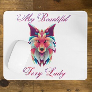 Pode incluir: Um tapete de rato branco com um design de raposa geométrico colorido e o texto "My Beautiful Foxy Lady".