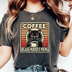 Könnte beinhalten: Ein schwarzes T-Shirt mit einer Grafik im Vintage-Stil, die eine schwarze Katze zeigt, die eine Kaffeetasse hält. Die Grafik lautet "Coffee because murder is wrong".