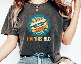 May include: A dark gray t-shirt with a vintage-style cassette tape graphic and the text "I'm this old".