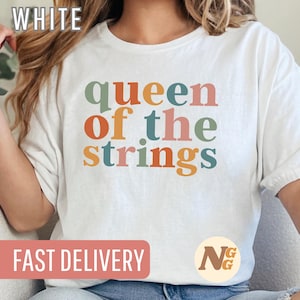 Könnte beinhalten: Weißes T-Shirt mit dem Text "queen of the strings" in bunten Buchstaben. Der Text ist in einer Schriftart im Retro-Stil.