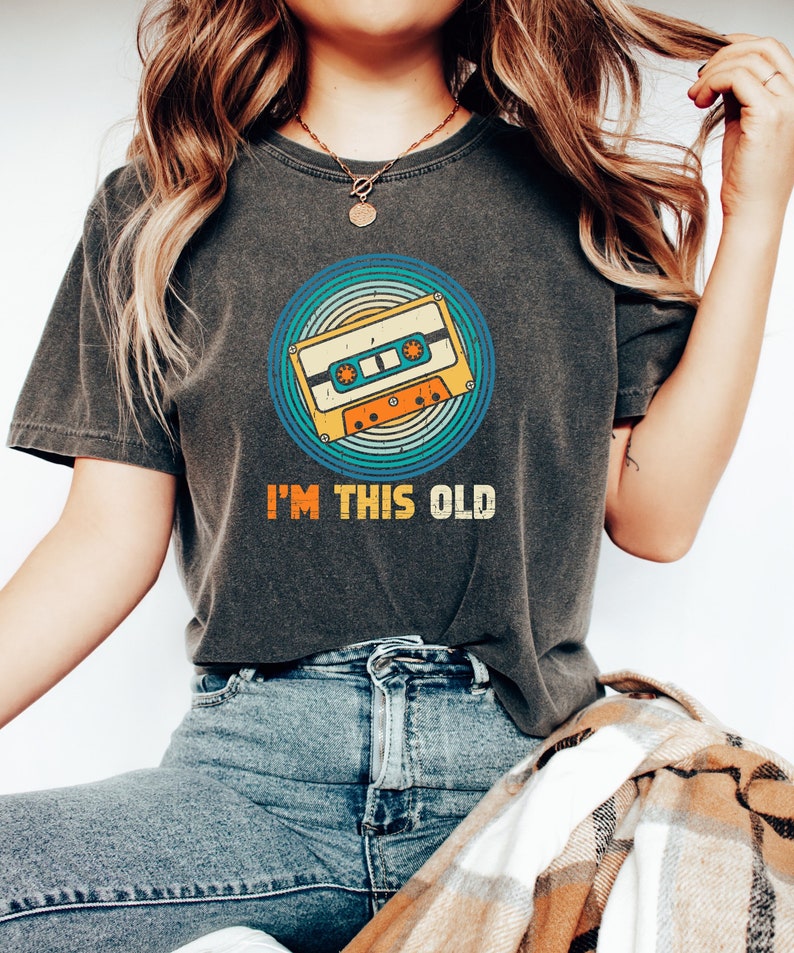May include: A dark gray t-shirt with a vintage-style cassette tape graphic and the text "I'm this old".