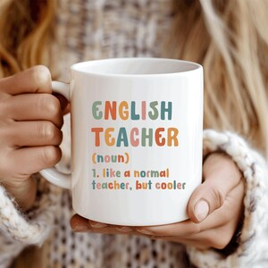 Könnte beinhalten: Weißer Keramikbecher mit den Worten "ENGLISH TEACHER" in bunten Buchstaben. Darunter die Definition: "1. wie ein normaler Lehrer, aber cooler."