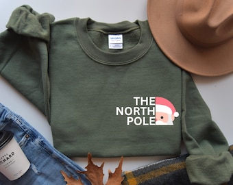 May include: A green sweatshirt with a white graphic that says "The North Pole" with a Santa Claus face replacing the "O" in "Pole".