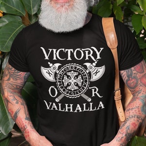 Könnte beinhalten: Ein schwarzes T-Shirt mit einem weißen Grafikdesign mit zwei gekreuzten Äxten, einem Schild mit Runen und dem Text "VICTORY OR VALHALLA".