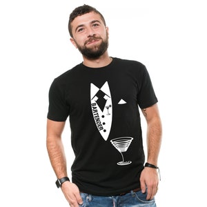 Pode incluir: Camiseta preta com um design de smoking branco e a palavra "BARTENDER" impressa na frente. O design do smoking inclui uma gravata borboleta, um lenço de bolso e uma taça de martini.