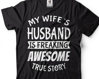 以下が含まれることがあります： 「My wife's husband is freaking awesome true story」という白い文字が書かれた黒いTシャツ。