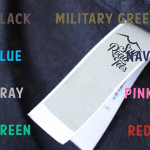Puede incluir: Una tabla de colores que muestra diferentes colores de camisetas, incluyendo negro, azul, gris, verde, verde militar, azul marino, rosa y rojo. La tabla tambi&eacute;n incluye una etiqueta blanca con el texto "Six Road Tees" y la palabra "NAVY".
