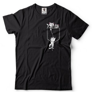 May include: Black t-shirt with a white pocket and three white cats. Two cats are peeking out of the pocket and one cat is hanging from a string.