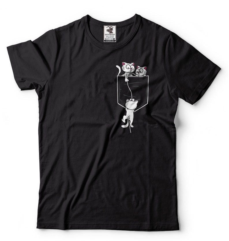May include: Black t-shirt with a white pocket and three white cats. Two cats are peeking out of the pocket and one cat is hanging from a string.