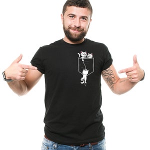 May include: A black t-shirt with a white graphic of two cats hanging from a pocket. The cats are looking out of the pocket.