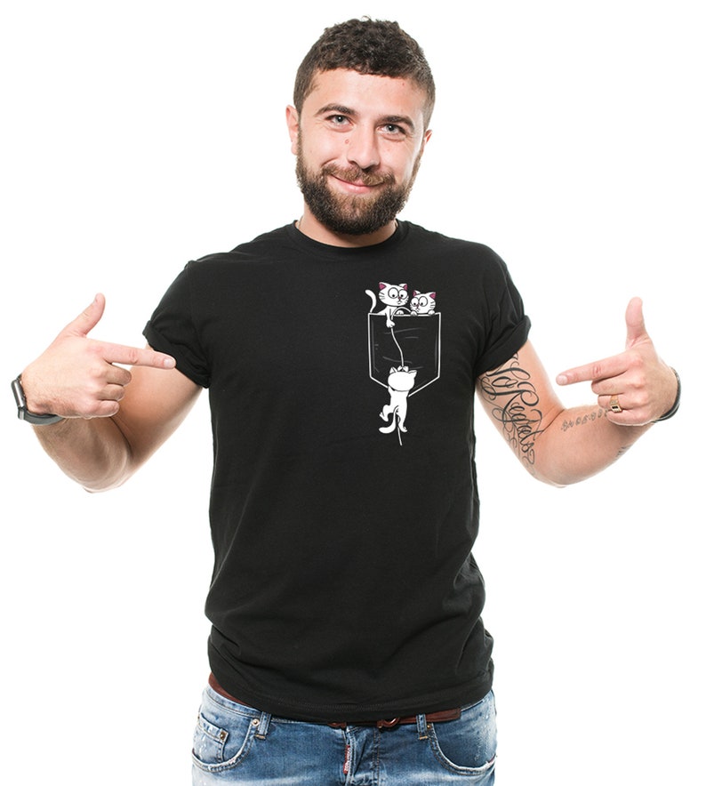 May include: A black t-shirt with a white graphic of two cats hanging from a pocket. The cats are looking out of the pocket.