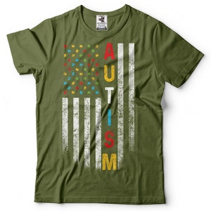 Puede incluir: Una camiseta verde con un dise&ntilde;o de bandera estadounidense desgastado. La bandera est&aacute; compuesta por piezas de rompecabezas en rojo, azul, amarillo y verde. La palabra "AUTISMO" est&aacute; escrita verticalmente en la bandera en blanco.