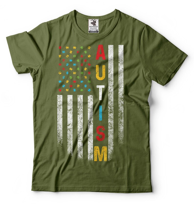 Puede incluir: Una camiseta verde con un dise&ntilde;o de bandera estadounidense desgastado. La bandera est&aacute; compuesta por piezas de rompecabezas en rojo, azul, amarillo y verde. La palabra "AUTISMO" est&aacute; escrita verticalmente en la bandera en blanco.