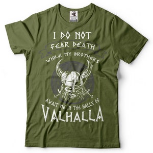 Puede incluir: Camiseta verde con un estampado gr&aacute;fico blanco de un guerrero vikingo con un casco con cuernos y empu&ntilde;ando espadas. El texto dice "No temo la muerte mientras mis hermanos me esperan en las salas de Valhalla."
