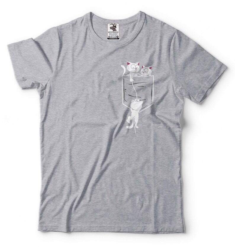 May include: A gray t-shirt with a white pocket and three white cats drawn on it. The cats are peeking out of the pocket, with one hanging from the top of the pocket.