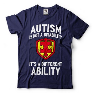 May include: Navy blue t-shirt with white text that reads "Autism is not a disability it's a different ability". A red and yellow puzzle piece is in the center of the shirt.