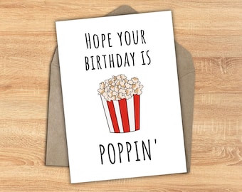 May include: White card with black text that reads "Hope your birthday is poppin'" and a cartoon image of a red and white striped popcorn bucket with popcorn inside.