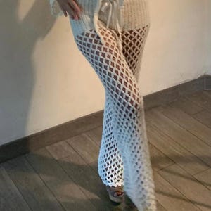 Peut inclure: Pantalon en crochet blanc avec un motif ajouré en forme de losange. Le pantalon a une jambe évasée et une taille à cordon. Le pantalon en crochet est un vêtement léger et aéré.