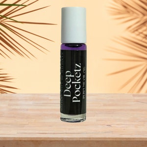 May include: A clear glass roller bottle with a white cap. The bottle is filled with a purple liquid and has a black label that reads "Deep Pocketz Perfume Oil 10 ml".