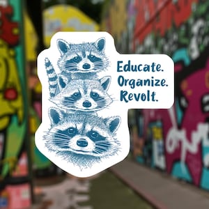 May include: A white sticker with a design of three blue raccoons, one above the other. The sticker has the words "Educate. Organize. Revolt." in blue text. The background is a blurred image of graffiti art.