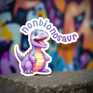 May include: A colorful sticker featuring a cartoon dinosaur with the text "nonbionosaur". The dinosaur is primarily purple with blue, orange, and red accents. The background is a blurred graffiti wall.