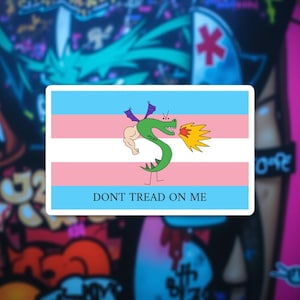 Op de afbeelding: Rechthoekige sticker met de transgender pride vlag en een cartoon groene draak die vuur spuwt. De draak heeft gespierde armen en paarse vleugels. De tekst "DONT TREAD ON ME" staat eronder.