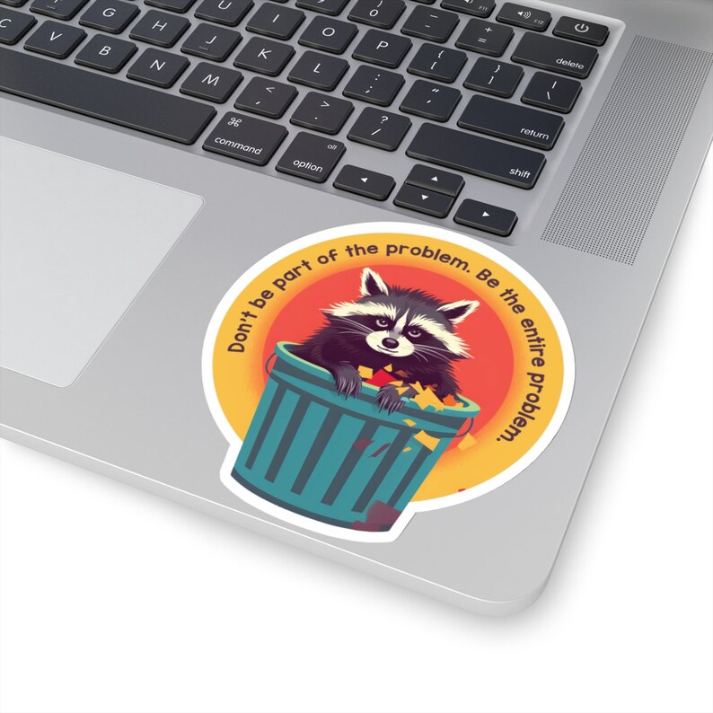 May include: A round sticker featuring a raccoon in a teal trash can, set against an orange and yellow background. The sticker has the text "Don't be part of the problem. Be the entire problem."