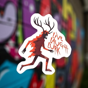 Könnte beinhalten: Ein Aufkleber mit einer cartoonartigen, rennenden Kreatur mit Geweih, einem schädelartigen Gesicht und roten Akzenten. Der Text "LIVE LAUGH LURK" ist in einer gezackten Schrift geschrieben. Der Aufkleber hat einen weißen Rand.