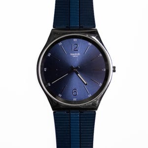 May include: A silver and blue Swatch watch with a blue face and a black and blue nylon strap.