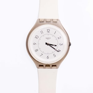 Può includere: Orologio Swatch bianco con cinturino bianco e quadrante argentato. Il quadrante ha numeri e lancette neri. L'orologio dice "Swatch Swiss" sul quadrante.