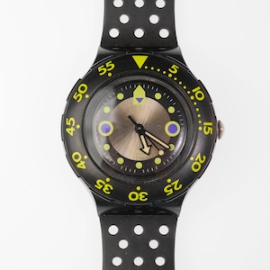 以下が含まれることがあります： 丸い文字盤と円形の切り欠きのある黒いストラップが付いた黒い腕時計。 文字盤はブロンズ色の中心部で、緑と青のアクセントが付いています。 ベゼルには緑色の数字とマーカーが付いています。