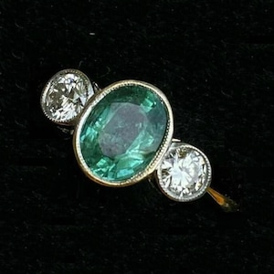 May include: A gold ring with a large oval emerald gemstone and two smaller round diamonds on either side.