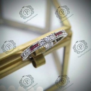 Könnte beinhalten: Ein zarter Ewigkeitsring mit einer Reihe kleiner runder Diamanten und einer Reihe rechteckiger Rubine, die in Weißgold gefasst sind.