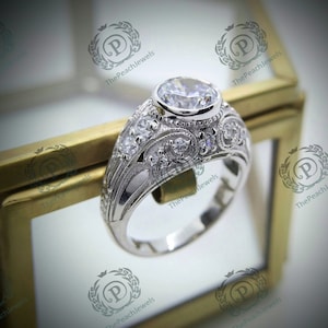 May include: A silver engagement ring with a large round center stone and smaller accent stones. The ring is set in a vintage-inspired design with intricate details.