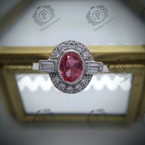 Peut inclure: Une bague en argent avec une pierre ovale rose entourée de petites pierres blanches. La bague a un design délicat avec deux pierres de forme baguette de chaque côté de la pierre centrale.