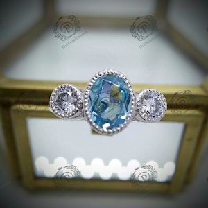 May include: A silver ring with three blue and white gemstones. The center stone is oval shaped and the two side stones are round.