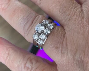 May include: A silver ring set with multiple clear round stones. The ring is worn on a person's finger.