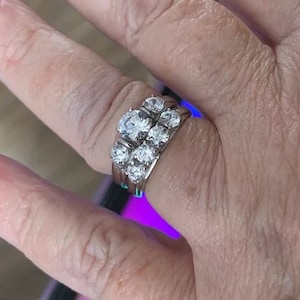 May include: A silver ring set with multiple clear round stones. The ring is worn on a person's finger.