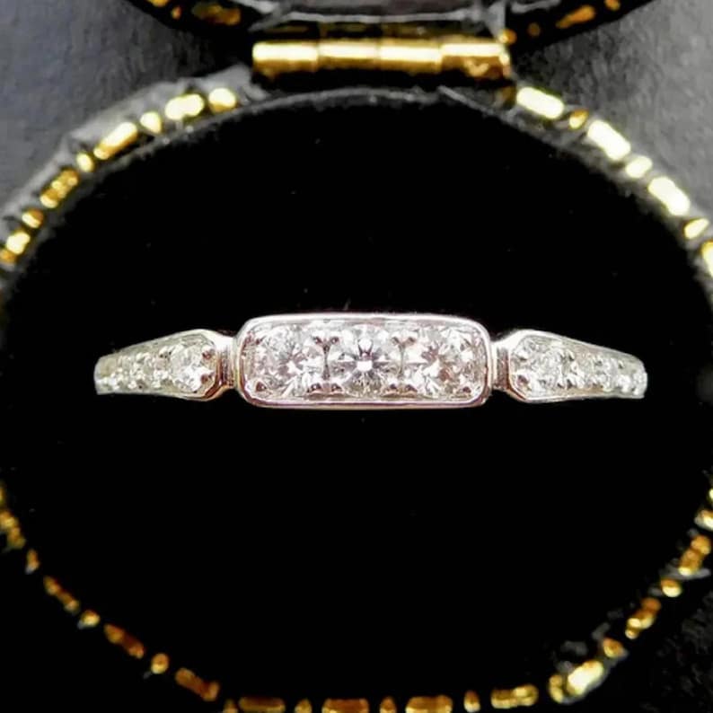 Puede incluir: Un anillo de banda de plata con una pieza central rectangular engastada con peque&ntilde;os diamantes. El anillo est&aacute; en una caja de anillo de terciopelo negro.