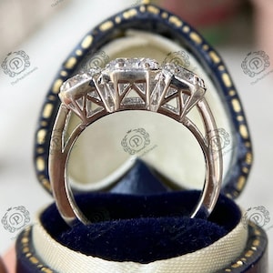 May include: A silver ring with three large, clear gemstones set in a prong setting. The ring is in a blue velvet ring box.