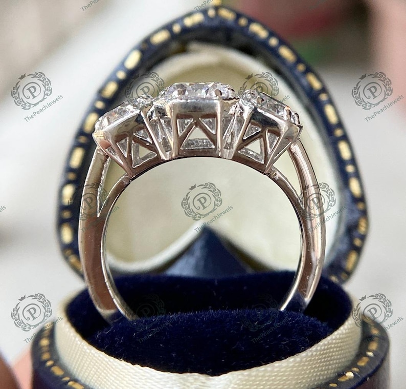 May include: A silver ring with three large, clear gemstones set in a prong setting. The ring is in a blue velvet ring box.