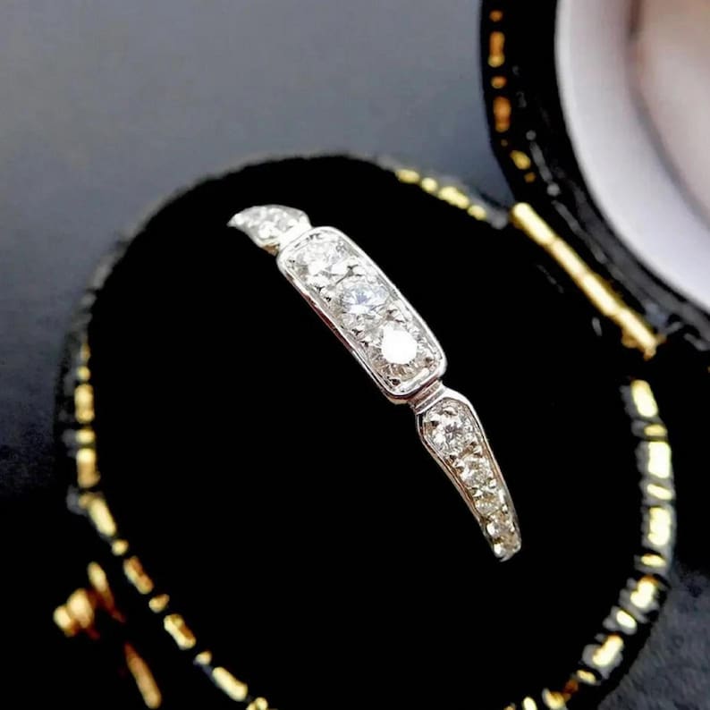 Puede incluir: Un anillo de banda de plata con una fila de peque&ntilde;os diamantes engastados en forma rectangular. El anillo se muestra en una caja de anillo de terciopelo negro.